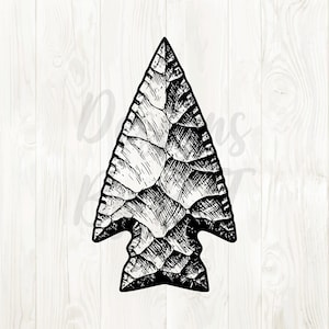May include: Black and white illustration of an arrowhead. The arrowhead is triangular with a notched base and a textured, stone-like appearance. The design is detailed, with visible lines and shading.