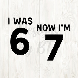 May include: Black text on a white wooden background reads "I WAS 6 NOW I'M 7". The numbers 6 and 7 are large and bold. The text is likely for a birthday or milestone celebration.