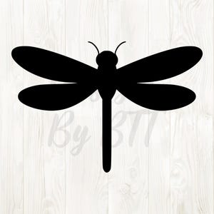 May include: A black silhouette of a dragonfly with outstretched wings. The dragonfly has a long, slender body and delicate wings. The image is set against a white wood grain background.