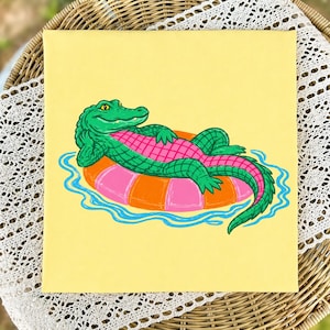 Op de afbeelding: Een vierkante canvas print met een groene alligator die ontspant op een roze en oranje opblaasbare ring in blauw water. De alligator heeft een roze buik en staat tegen een gele achtergrond. Het kunstwerk is in cartoonstijl.