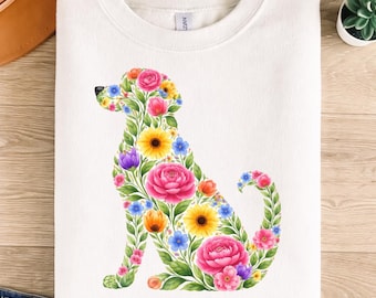 May include: White sweatshirt featuring a floral dog design. The dog silhouette is filled with colorful flowers, including pink roses, yellow sunflowers, and blue blossoms. The sweatshirt is folded on a wooden surface.