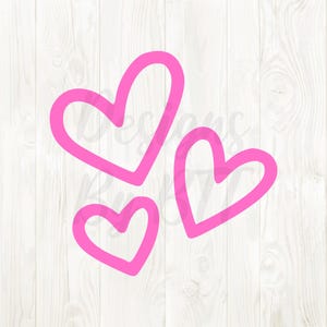 Pode incluir: Três formas de coração rosa de tamanhos variados são dispostas sobre um fundo branco com grão de madeira. Os corações têm um design simples e delineado, com uma cor rosa sólida preenchendo as bordas. A imagem tem uma estética limpa e minimalista.