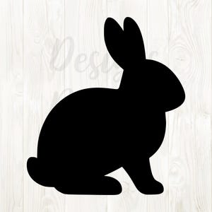 May include: A black silhouette of a rabbit in a seated position. The rabbit has long ears and a rounded body. The image is set against a white wood grain background.