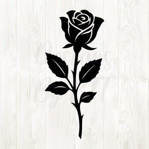 May include: A black rose silhouette with detailed petals and leaves. The rose is depicted on a stem with multiple leaves, creating a classic floral design. The image is set against a white wood grain background.
