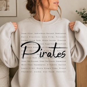 May include: A light gray crewneck sweatshirt featuring black text that reads: Team First. Individual Second. Dedicated. Early Practice. Late Film. Focused. Locker Room Talk. Stays Inside. Trusted. Win Together. Lose Together. Unified. Push Each Other. Lift Each Other. Strong. Sweat Equity. Paid In Full. Earned. One Game. Show Up Tomorrow. Resilient. Sacrifice Now. Celebrate Later. Patient. Trust The Process. Trust The Coach. Committed. More Than Teammates. A Family. Sacred. Leave It All. Every Single Time. Proud. Thankful. Lucky. One Team. Forever. The word Pirates is printed in a large, bold, black script font across the center.
