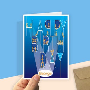 A birthday card with a blue gradient background and the words "HAPPY BIRTHDAY" in white and connected. The letters are filled with yellow stick figures having fun. Your recipient's name, in a yellow, in a white oval which radiates light like spotlights through the design. The hand holds the card next to a recycled brown envelope.