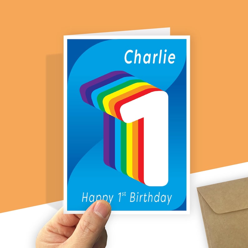 May include: A rectangular greeting card with a blue background featuring a large, white, three-dimensional number one with a rainbow-colored side profile. The text Charlie is printed at the top, and Happy 1st Birthday is printed at the bottom.