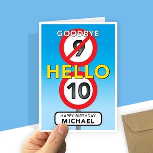 A personalised 10th birthday card with a light blue gradient background featuring road-sign style graphics. At the top, a red-bordered circle with a diagonal line through the number 9 is labeled "GOODBYE" above it. In the centre, the word "HELLO" is written in large yellow text, followed by a second red-bordered circle containing the number 10. At the bottom, a white rectangular sign with rounded corners reads "HAPPY BIRTHDAY your recipient's name."