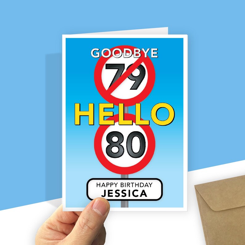 A personalised 80th birthday card with a light blue gradient background featuring road-sign style graphics. At the top, a red-bordered circle with a diagonal line through the number 79 is labeled "GOODBYE" above it. In the centre, the word "HELLO" is written in large yellow text, followed by a second red-bordered circle containing the number 80. At the bottom, a white rectangular sign with rounded corners reads "HAPPY BIRTHDAY your recipient's name."