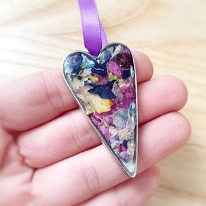 May include: A silver heart-shaped pendant with a clear resin filling containing pressed flowers in shades of pink, purple, blue, and yellow.