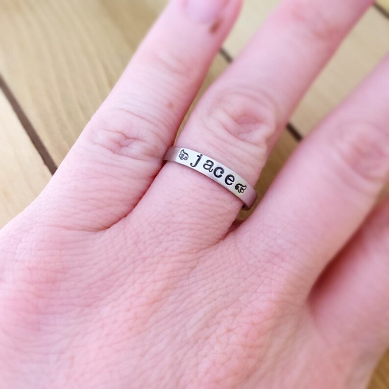 May include: A silver ring with the name "Jace" engraved on it. The ring is worn on a person's finger.