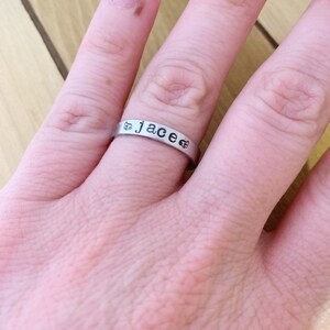 May include: A silver ring with the name "Jace" engraved on it. The ring is worn on a person's finger.