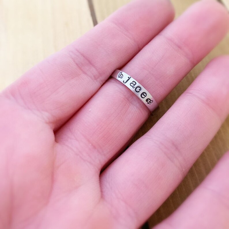 May include: A silver ring with the name "Jace" engraved on it. The ring is on a person's finger.