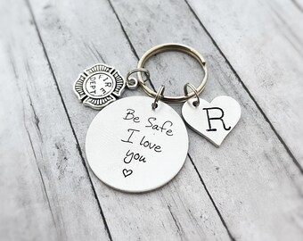 May include: Silver keychain with a round charm that says "Be Safe I love you" with a heart at the bottom. There is a small silver firefighter charm and a heart charm with the letter "R" on it.