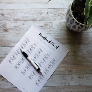 Puede incluir: Un gráfico de diadema imprimible con un bolígrafo negro encima. El gráfico tiene un título que dice "Headband Chart" y tiene una cuadrícula de formas de lazo.