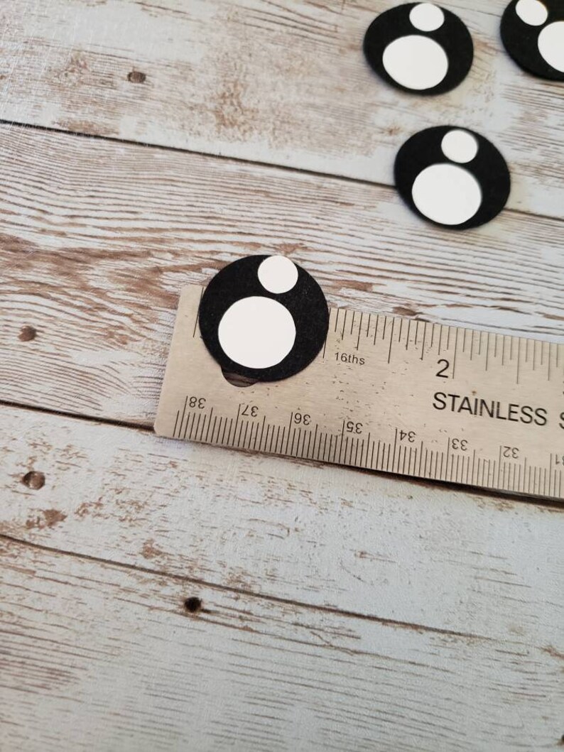 May include: Black and white felt circles with a smaller white circle inside the larger circle. The circles are measured against a ruler with 16ths of an inch markings.
