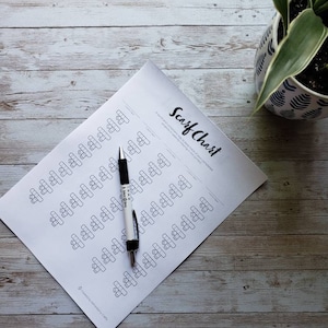 Puede incluir: Una hoja de papel blanca con el título "Scarf Chart" y una cuadrícula de cuadrados con líneas dibujadas en su interior. Un bolígrafo blanco y negro está sobre el papel.