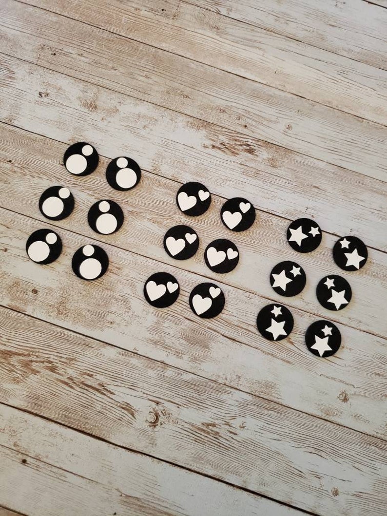Puede incluir: Un conjunto de fichas de juego circulares en blanco y negro con diferentes s&iacute;mbolos. Los s&iacute;mbolos incluyen un c&iacute;rculo, un coraz&oacute;n y una estrella.