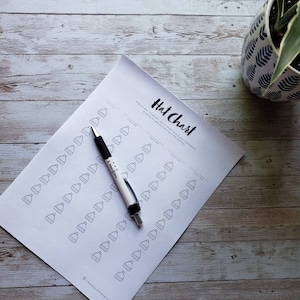 Puede incluir: Un gráfico de sombreros imprimible con el texto "Hat Chart" en la parte superior. El gráfico está diseñado para llevar un registro de la cantidad de sombreros que se usan cada día. Un bolígrafo está sobre el gráfico.