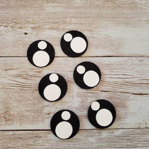 May include: Six black circles with white circles inside, each with a smaller white circle inside the larger white circle. The circles are arranged in a semi-circle pattern on a light brown wooden surface.