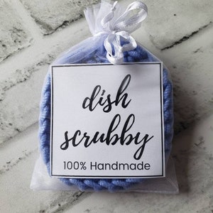 May include: A blue dish scrubby in a white organza bag with a white ribbon. The bag has a white tag with black text that reads "dish scrubby 100% Handmade".
