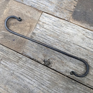 May include: A black metal hook with two loops at each end. The hook is lying on a wooden surface.