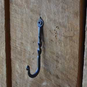 May include: A black metal hook with a twisted design is screwed into a wooden surface.