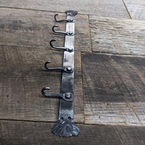 May include: A black metal hook rack with five hooks. The rack is mounted on a wooden surface.