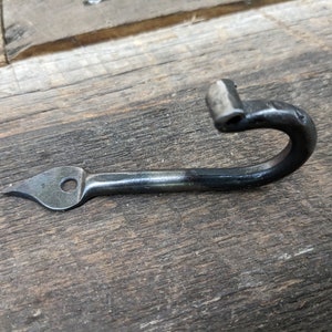 May include: A black metal hook with a pointed end and a curved hook. The hook is made of wrought iron and has a rustic finish.