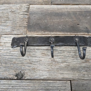 May include: A black metal hook rack with three hooks. The rack is mounted on a wooden surface.