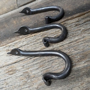May include: Three black metal hooks with a unique curved design. The hooks are mounted on a wooden surface.