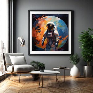 Puede incluir: Obra de arte enmarcada que representa a un astronauta con un traje espacial frente a un planeta vibrante con tonos naranja, azul y amarillo. El astronauta es el punto focal, colocado contra una pared gris oscuro en un salón moderno.