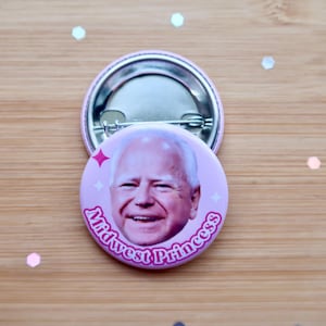May include: A pink button with a picture of a man with white hair and a pink background. The text "Midwest Princess" is written in pink letters around the edge of the button.
