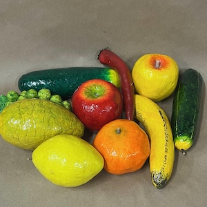 May include: A group of colorful fruits and vegetables, including a red apple, a yellow lemon, a yellow banana, a green cucumber, a red chili pepper, a yellow apple, a green lime, and an orange.