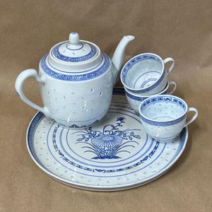 May include: A white porcelain tea set featuring blue geometric and floral patterns. The set includes a teapot with a lid, two teacups, and a round serving tray. Each piece displays a delicate pierced lattice design throughout the white ceramic surface.