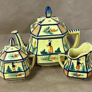 May include: A yellow ceramic tea set with a teapot, sugar bowl, and creamer. Each piece features a geometric design with orange, green, and blue accents, and a painted scene of a person in a landscape. The set has a vintage aesthetic.
