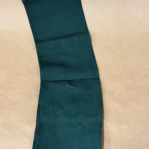 May include: Dark green denim pants folded neatly. The pants are a solid color and appear to be made of a durable fabric. The image shows the pants from the waist to the knees.