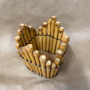 May include: A heart-shaped bamboo basket. The basket is constructed from numerous small bamboo stalks held together with black bands. The bamboo has a natural, light brown color, and the ends of the stalks are visible.