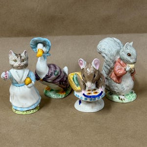 May include: A collection of ceramic figurines featuring animal characters. The figurines include a cat, a goose, a mouse, and a squirrel. The cat holds a sign that says "Soap". The squirrel wears a red jacket and holds a snack.
