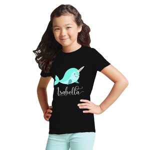 K&ouml;nnte beinhalten: Schwarzes T-Shirt mit einem Cartoon-Narwal und dem Namen "Isabella" darauf gedruckt.