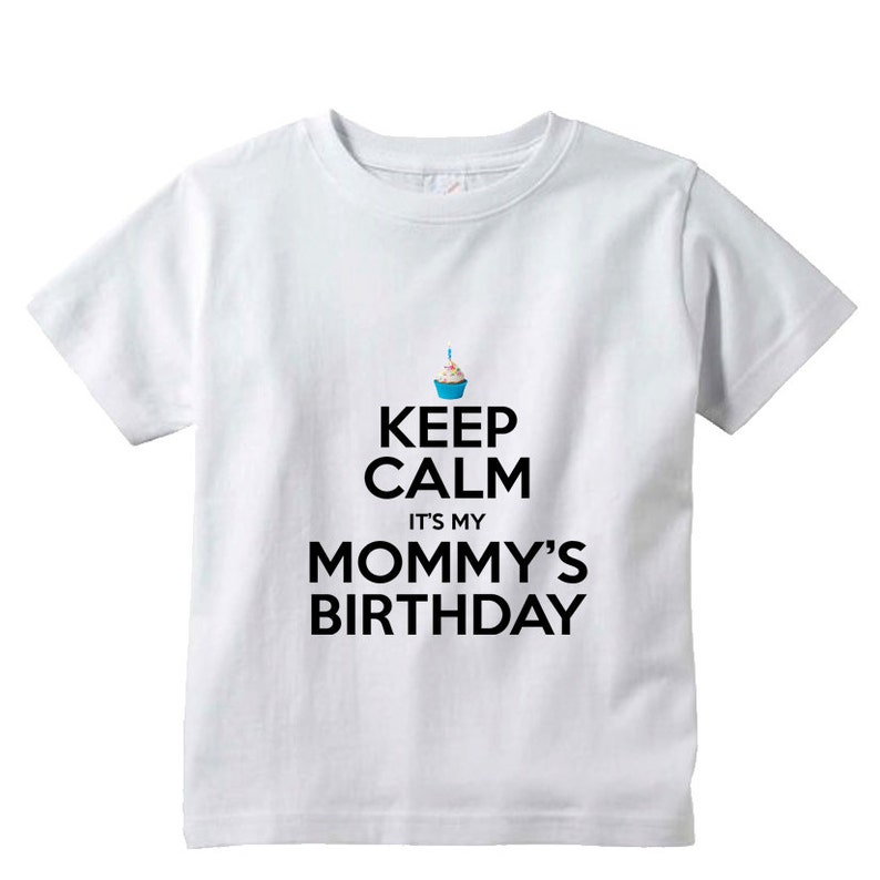 May include: White t-shirt with black text that reads "Keep Calm It's My Mommy's Birthday". A small blue cupcake with a lit candle is above the text.