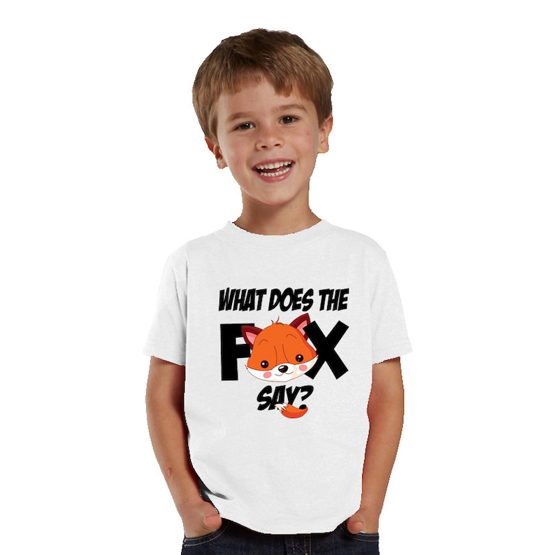 Może przedstawiać: Biała koszulka z czarnym napisem "WHAT DOES THE FOX SAY?" oraz grafiką z kresk&oacute;wkowym lisem w kolorze pomarańczowym, białym i brązowym. Koszulka jest noszona przez małe dziecko.