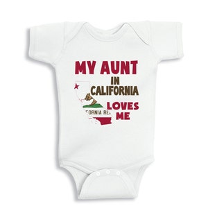 May include: White baby onesie with a red graphic that says "My Aunt in California Loves Me". The graphic also includes a stylized outline of the state of California with the California state flag inside.