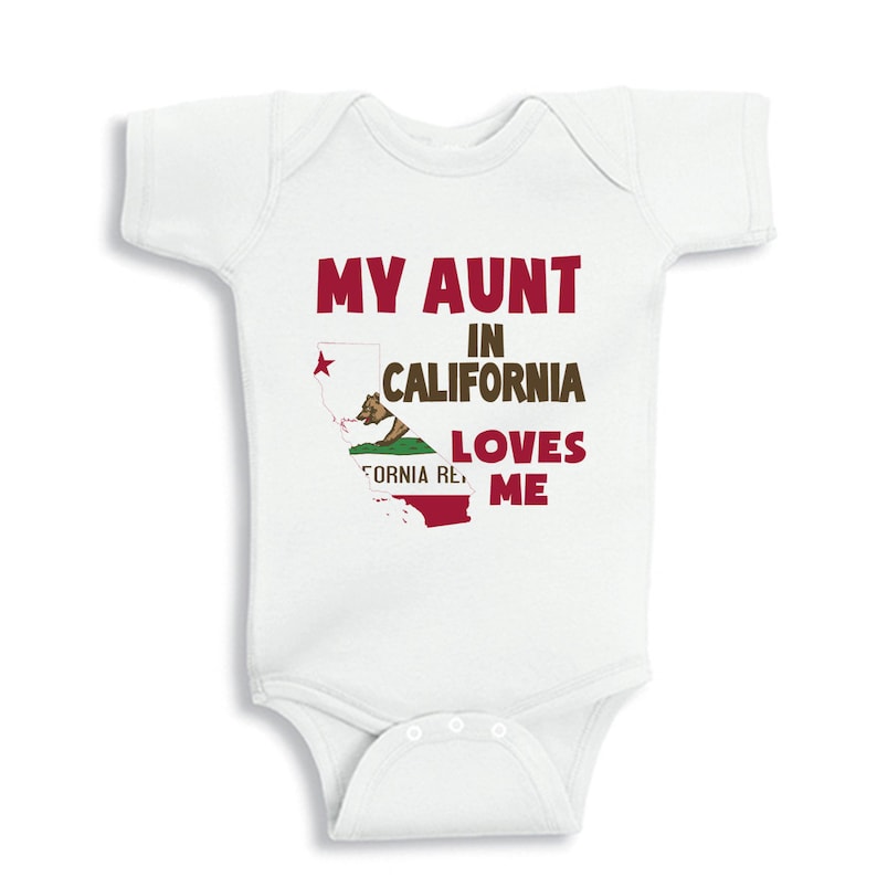 May include: White baby onesie with a red graphic that says "My Aunt in California Loves Me". The graphic also includes a stylized outline of the state of California with the California state flag inside.