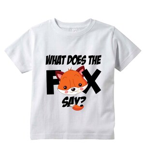 Może przedstawiać: Biała koszulka z kresk&oacute;wkowym lisem i napisem "WHAT DOES THE FOX SAY?". Lis jest pomarańczowy z czarno-białymi akcentami. Tekst jest czarny, ze znakiem zapytania w kolorze ogona lisa.
