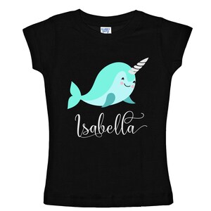 K&ouml;nnte beinhalten: Schwarzes T-Shirt mit einem hellblauen Narwal mit einem silbernen Horn und dem Namen "Isabella" in wei&szlig;er Kursivschrift.