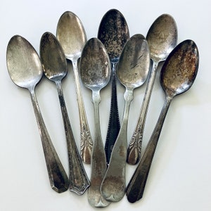 May include: A collection of eight vintage silver spoons with ornate designs. The spoons are arranged in a fan shape, with the handles pointing outwards.
