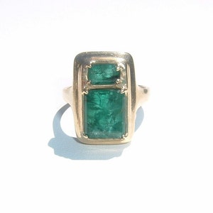 May include: A gold ring featuring two emerald green rectangular gemstones set in a gold frame.