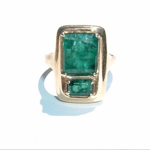 May include: A gold ring with two emerald green gemstones set in a rectangular frame.