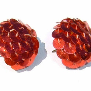 May include: A pair of red sequined earrings. Each earring is a cluster of small, round sequins that are arranged in a dome shape.